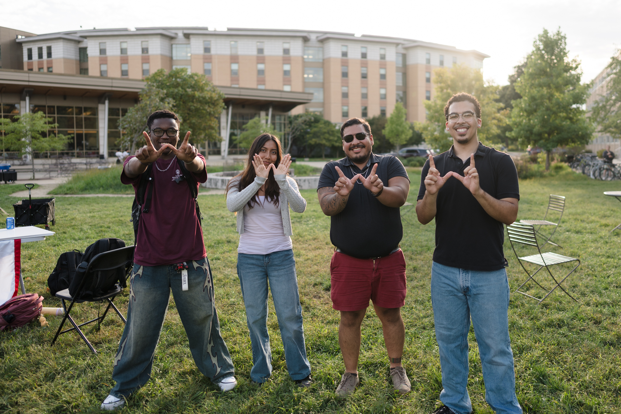 Four people standing on a lawn in front of a building making a W with their hands. 
